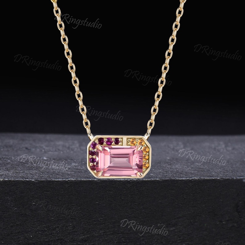 May include: A delicate gold chain necklace with a pink gemstone pendant surrounded by smaller pink, purple, and yellow gemstones.