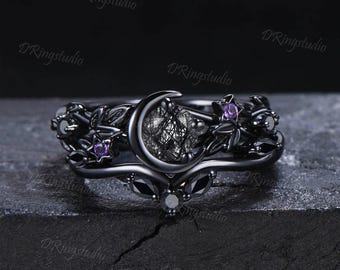 May include: Black ring set with a crescent moon design, featuring a black rutilated quartz stone, black and purple gemstones, and intricate floral details.