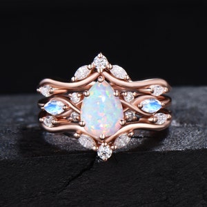 May include: A rose gold ring set with a pear-shaped opal and smaller clear and blue stones. The ring is designed with a delicate, intricate pattern.