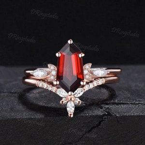Könnte beinhalten: Ein Verlobungsring aus Roségold mit einem großen roten Edelstein und kleineren weißen Edelsteinen. Der Ring hat ein zartes Blumenmuster.