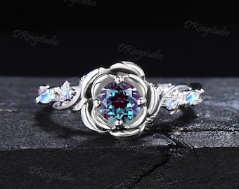 Puede incluir: Un anillo de plata con una gran piedra preciosa redonda e iridiscente engastada en un diseño en forma de rosa. La banda está adornada con piedras preciosas más pequeñas y transparentes.