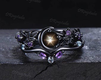 May include: Black ring set with a celestial theme, featuring a crescent moon and starburst design. The rings are decorated with purple and blue gemstones, and detailed floral and star motifs. A unique and elegant jewellery piece.