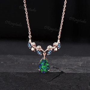 May include: A delicate rose gold necklace with a pear-shaped green opal pendant and blue gemstone accents. The necklace features a delicate branch design with leaves.