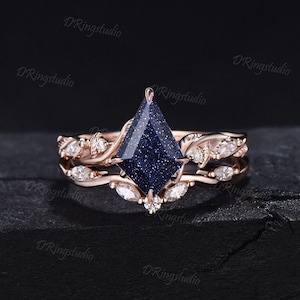 May include: A rose gold engagement ring set with a blue gemstone and a matching band with delicate leaf details and small diamonds.
