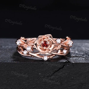 May include: Rose gold ring with a red gemstone rose and white pearl accents. The ring features a delicate vine design.