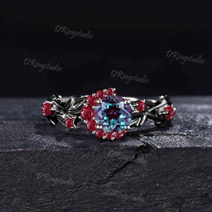 May include: A black ring with a large, round, iridescent gemstone surrounded by smaller red gemstones. The ring features a leafy design.