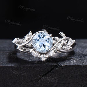 May include: A delicate silver ring with a large, round aquamarine gemstone surrounded by smaller diamonds. The ring features a leafy design with intricate details.