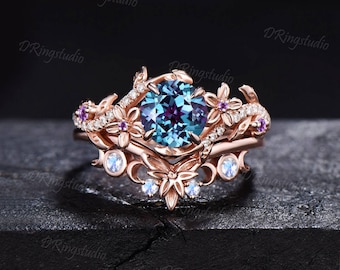 Könnte beinhalten: Ein Verlobungsring aus Roségold mit einem großen blauen und violetten Alexandrit-Edelstein, der von kleineren Diamanten und rosa Saphiren umgeben ist. Der Ring hat ein zartes Blumenmuster mit Blättern und Blüten.