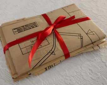 May include: A stack of brown paper sewing patterns tied together with a red ribbon. The patterns are labeled with the number 1432 and the text "WE REVILED PAPER FOR OUR PATTERN PRODUC", "CTS", and "NECYSLE PAR PATRONG".