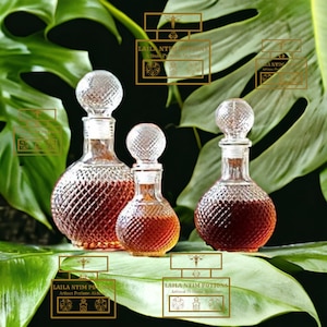 Peut inclure: Trois flacons en verre à surface texturée remplis d'un liquide brun foncé. Les flacons sont posés sur une feuille verte. Les flacons portent une étiquette dorée avec le texte "LAILA NTIM POTIONS Artisan Perfume Alchemy".