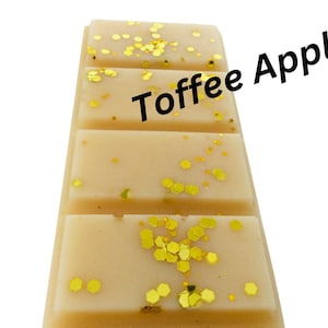 May include: A light tan wax melt bar, divided into four sections, with gold glitter scattered across the surface. The text "Toffee Apple" is printed diagonally across the bar.