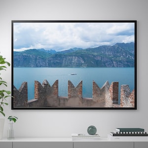 Può includere: Una fotografia incorniciata di una vista panoramica di un lago con montagne sullo sfondo. Il lago è di colore blu chiaro e le montagne sono di colore verde scuro. La foto è stata scattata da un punto di vista elevato, con vista sul lago. Ci sono muri di pietra in primo piano.