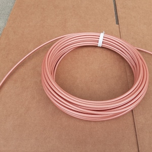 May include: A coil of pink coaxial cable, wrapped around itself on a brown surface.