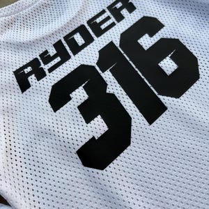 K&ouml;nnte beinhalten: Wei&szlig;es Mesh-Trikot mit schwarzem Text "Ryder 316".