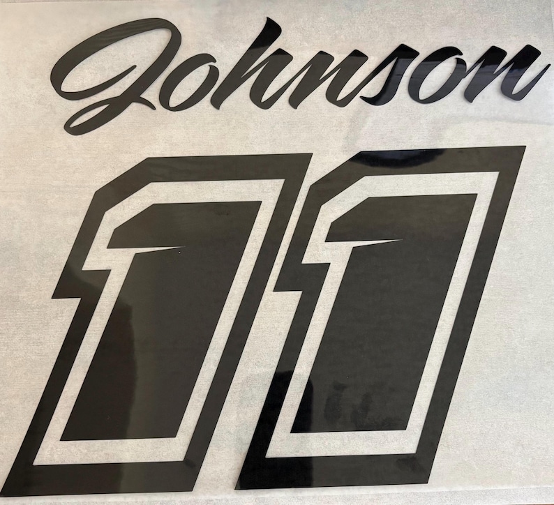 K&ouml;nnte beinhalten: Schwarzer Vinyl-Aufkleber mit dem Namen "Johnson" und der Nummer "11" in einer fetten, umrandeten Schrift.