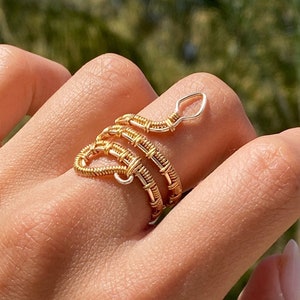 May include: A gold and silver wire wrapped snake ring. The ring is coiled around a finger and the tail of the snake is curled up.