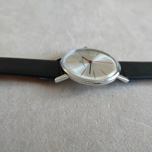May include: A silver wristwatch with a white face and black leather band. The watch has a red second hand and gold accents.