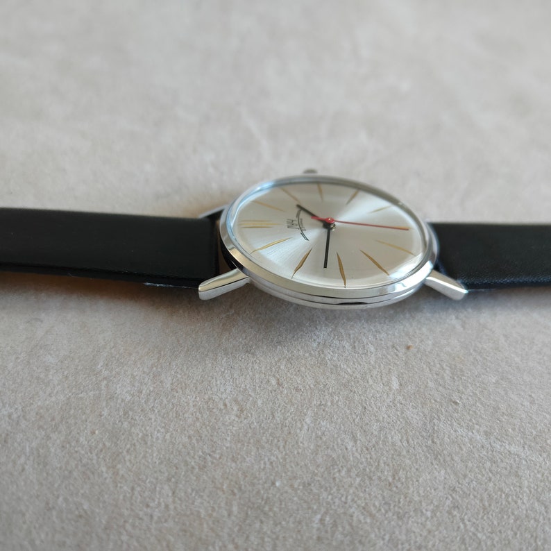 May include: A silver wristwatch with a white face and black leather band. The watch has a red second hand and gold accents.