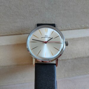 May include: A silver wristwatch with a white face and black leather band. The watch face has gold-colored markings and the word "Луч" in Cyrillic script.