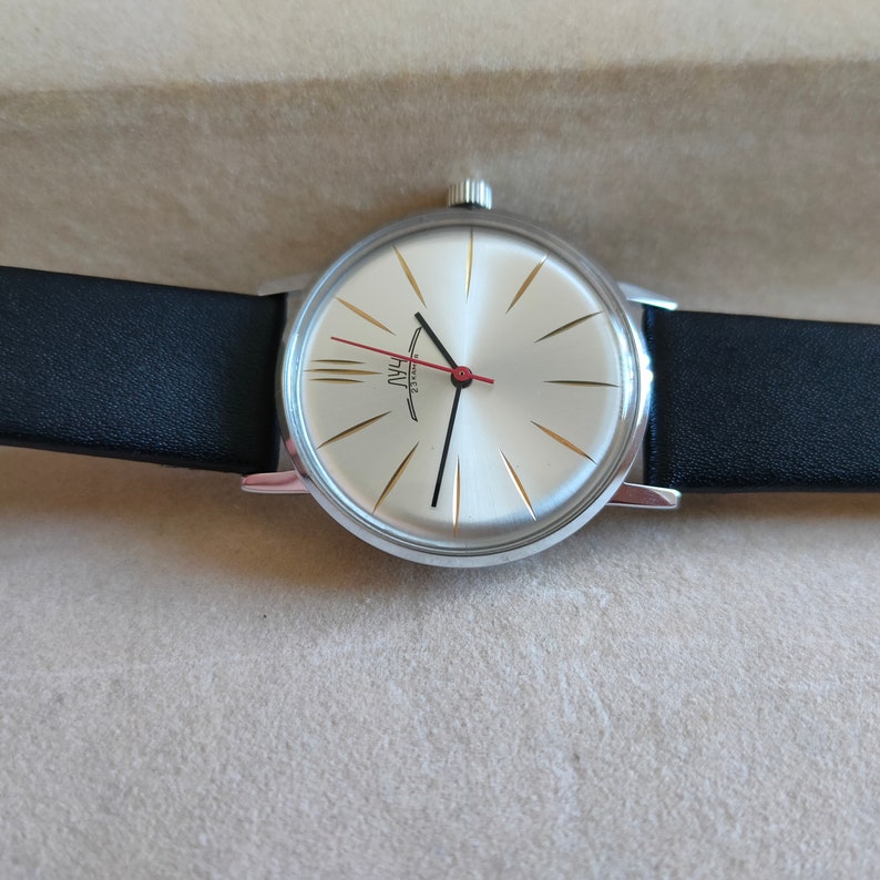 May include: A silver wristwatch with a white face and black leather band. The watch face has gold-colored hour markers and a red second hand. The watch face also has the text "USSR" and "ЧACOBЫE" printed on it.