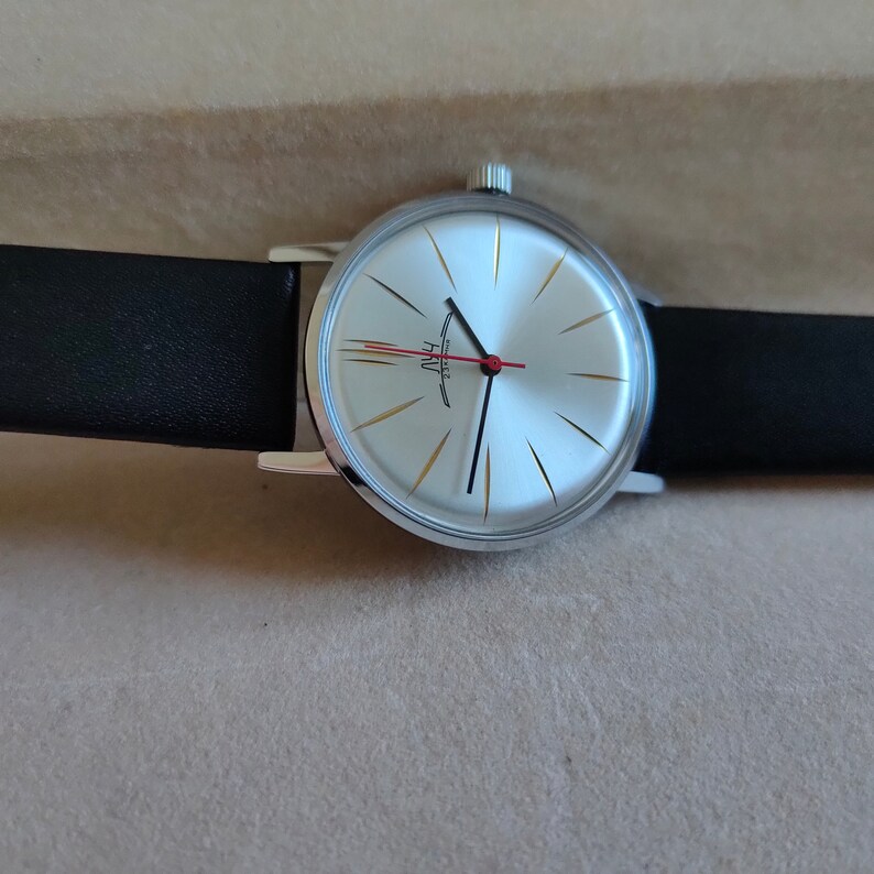 May include: A silver wristwatch with a white face and gold accents. The watch has black hands and a red second hand. The watch is on a black leather band.