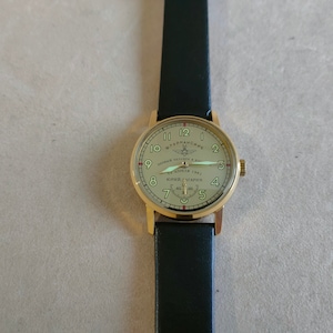 Puede incluir: Un reloj de pulsera dorado con una correa de cuero negro. La esfera del reloj es blanca con marcas negras y presenta el texto "ШТУРМАНСКИЕ" y "ПЕРВЫЙ ЧЕЛОВЕК В КОСМОСЕ" con una estrella roja y un peque&ntilde;o gr&aacute;fico de avi&oacute;n. El texto "12 АПРЕЛЯ 1961" y "ЮРИЙ ГАГАРИН" tambi&eacute;n est&aacute; en la esfera del reloj.