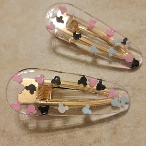 May include: Two clear plastic hair clips with gold metal clasps. The clips are decorated with small, colourful Mickey Mouse heads.