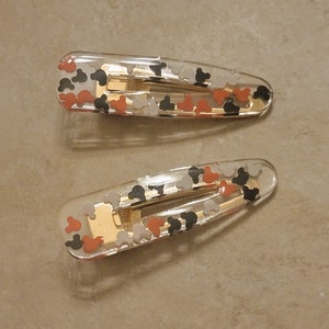 May include: Two clear plastic hair clips with a gold metal spring. The clips are decorated with small, colourful Mickey Mouse heads.