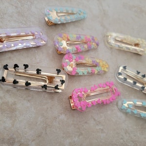 May include: A set of ten clear plastic hair clips with different coloured designs. The designs include pink, yellow, blue, and black Mickey Mouse heads.