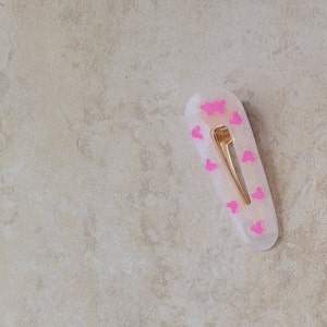May include: A white hair clip with a gold metal bar and pink Mickey Mouse silhouettes.