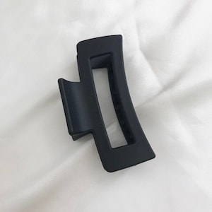 May include: A black plastic hair clip with a curved shape and a rectangular opening.