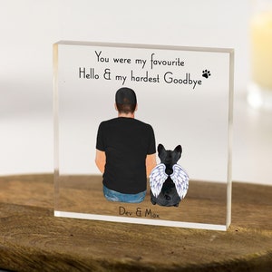 May include: A clear acrylic block with a black and white illustration of a person and a dog with angel wings. The text reads "You were my favourite Hello & my hardest Goodbye" with paw prints. The bottom of the block reads "Dev & Max".