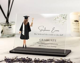 May include: A clear acrylic plaque with a black base, featuring a graduate in a black cap and gown holding a diploma and a champagne bottle. The text reads "Stephanie Evans, She believed she could so she did! GRADUATE, Northampton University, BSc (Hons) Adult Nursing."