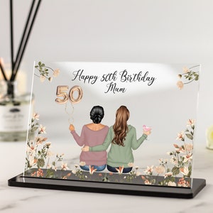 Könnte beinhalten: Eine durchsichtige Acrylplatte mit einem Blumendesign und zwei Frauen, die Rücken an Rücken sitzen. Die Platte trägt den Text "Happy 50th Birthday Mum" und einen goldenen Ballon mit der Nummer 50.