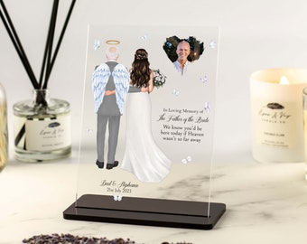 May include: A clear acrylic memorial plaque with a white background and a watercolor illustration of a bride and a man with angel wings. The man is wearing a gray suit and the bride is wearing a white dress. The plaque has a black base and the text "In Loving Memory of The Father of the Bride We know you'd be here today if Heaven wasn't so far away Dad & Stephanie 21st July 2023" is printed on the plaque.