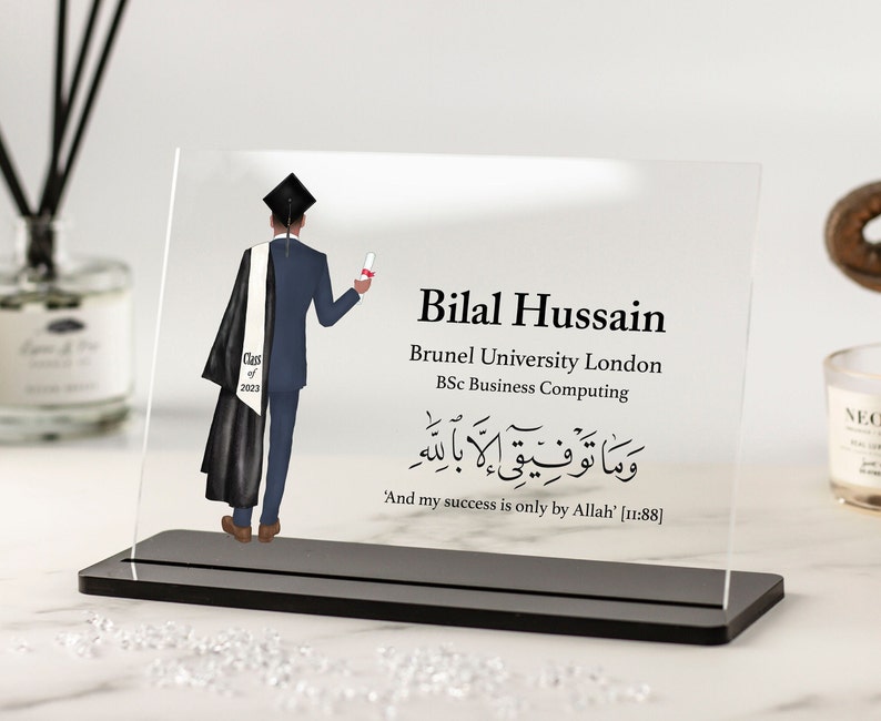 May include: A clear acrylic plaque with a black stand, featuring a cartoon illustration of a graduate in a cap and gown. The plaque includes the text "Bilal Hussain", "Brunel University London", "BSc Business Computing", and an Arabic inscription with the translation "And my success is only by Allah [11:88]".