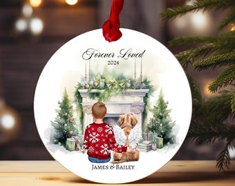 Può includere: Un addobbo natalizio rotondo bianco con un'illustrazione ad acquerello di un ragazzo e un cane seduti vicino a un camino. L'addobbo ha il testo "Forever Loved 2024" e "James & Bailey".