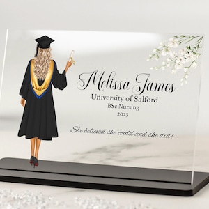 Peut inclure: Une plaque en acrylique transparente avec une base noire, représentant une diplômée portant une toge et un bonnet noirs, tenant un diplôme. Le texte indique "Melissa James, Université de Salford, BSc Nursing, 2023, She believed she could and she did!"