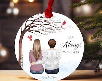 May include: A round white ornament with a winter scene featuring two figures with angel wings, a tree with red birds, and the text "I am Always With You". The ornament also includes the text "Libby & Mum".