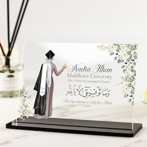May include: A clear acrylic plaque with a black base, featuring a black and white illustration of a woman in a graduation cap and gown. The text "Nadia Khan, Middlesex University, BSc (Hons) Accounting & Finance, وما توفيقي إلا بالله, And my success is only by Allah' [11:88/" is printed on the plaque.