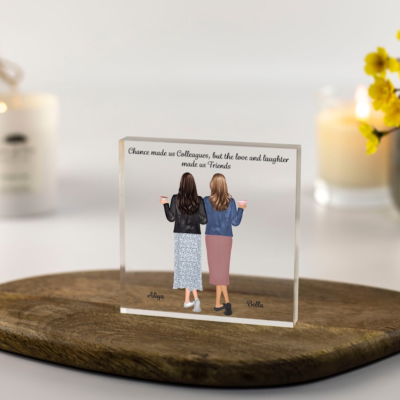 Puede incluir: Un bloque de acr&iacute;lico transparente con una cita sobre la amistad y dos mujeres ilustradas sosteniendo tazas de caf&eacute;. La cita dice "La casualidad nos hizo colegas, pero el amor y la risa nos hicieron amigos". Los nombres "Aliya" y "Bella" est&aacute;n escritos debajo de las mujeres.