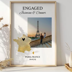 May include: Framed print with the text "ENGAGED Jasmine & Connor" above a photo of the Eiffel Tower in Paris. A map of France with a heart marking a location is below the photo. The text "PARIS, FRANCE 20.07.25" is at the bottom.