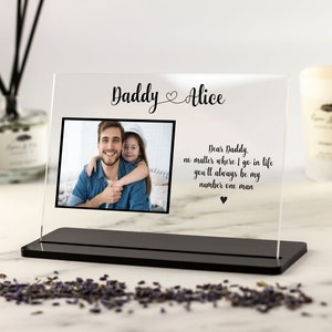 May include: A clear acrylic photo frame with a black base. The frame holds a photo of a father and daughter. The text "Daddy Alice" is printed at the top of the frame. The text "Dear Daddy, no matter where I go in life you'll always be my number one man" is printed below the photo.