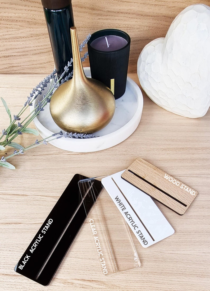 May include: Three different display stands for products. A black acrylic stand, a clear acrylic stand, and a wood stand. Each stand has the name of the stand printed on it in white text.