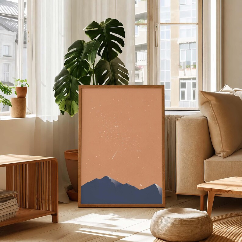 May include: A rectangular framed wall art print featuring a minimalist landscape illustration with dark blue mountain silhouettes against a solid terracotta orange sky filled with white stars and a small crescent moon in the lower right corner.