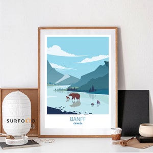 May include: A framed art print featuring a stylized landscape of Banff, Canada. The artwork depicts a bear and cub wading in a lake, with mountains in the background. The color palette includes shades of blue, green, and brown.