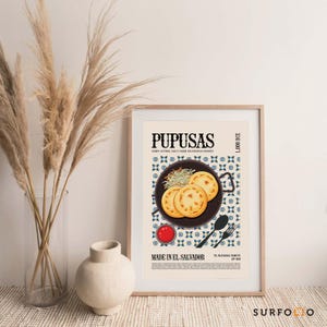May include: A framed poster featuring the word "PUPUSAS" at the top. The poster includes an illustration of pupusas on a plate, a small bowl of sauce, and text that reads "MADE IN EL SALVADOR". The poster is in a wooden frame.