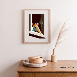 Op de afbeelding: Een ingelijste illustratie van een persoon die in een raam zit met een kopje koffie en een hangende plant. Het raam is omlijst met hout en de illustratie is in een minimalistische stijl.