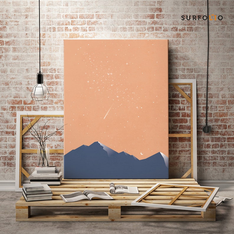 Pode incluir: Uma impress&atilde;o de arte digital que apresenta uma paisagem estilizada com uma cordilheira silhueta contra um c&eacute;u cor de p&ecirc;ssego com estrelas brancas e uma estrela cadente. A impress&atilde;o &eacute; exibida em uma plataforma de madeira com outros itens.