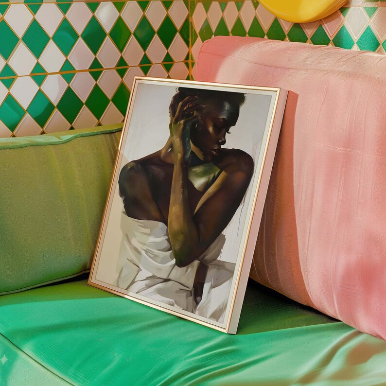 May include: A framed art print featuring a portrait of a person with dark skin, draped in white fabric. The artwork has a gold frame and is displayed on a green surface, with a pink cushion in the background. The art style is painterly.